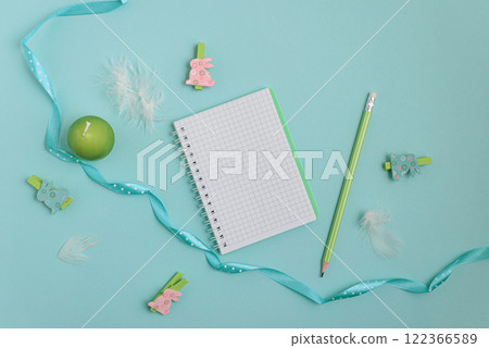 A pastel Easter scene featuring a bouquet of pink tulips adorned with a delicate blue ribbon, a notebook, wooden rabbit figurines, and soft feathers. Perfect for celebrating the Easter holiday. 122366589