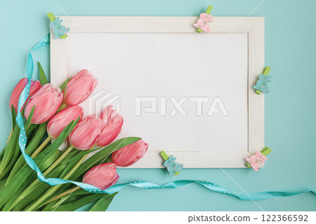 A vibrant Easter greeting card featuring a delicate arrangement of pink tulips, a soft blue ribbon, and adorable bunny-shaped clothespins. Perfect for spreading joy and warmth this Easter season. 122366592