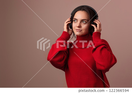 Happy woman wearing red sweater and headphones enjoying listening music on pink background. Happy woman wearing red sweater and headphones enjoying listening music on pink background. 122366594