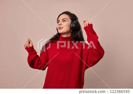 Happy woman wearing red sweater and headphones enjoying listening music and dancing on pink background. Happy woman wearing red sweater and headphones enjoying listening music and dancing on pink background. 122366595