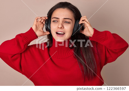 Happy woman wearing red sweater and headphones enjoying listening music on pink background. 122366597
