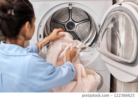 woman put pastel cotton towel in automatic washing machine with open door 122366625