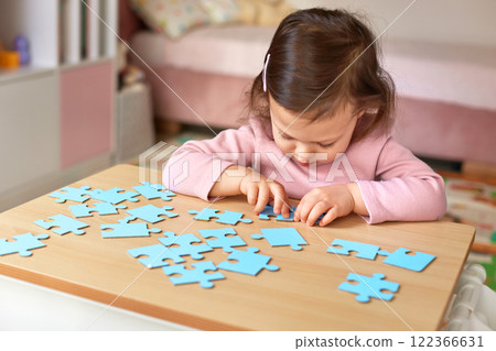 Cute little child girl connecting puzzle pieces on wooden desk in room, children development 122366631