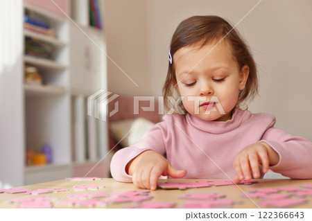 Cute little child girl solving puzzles on wooden desk at home 122366643