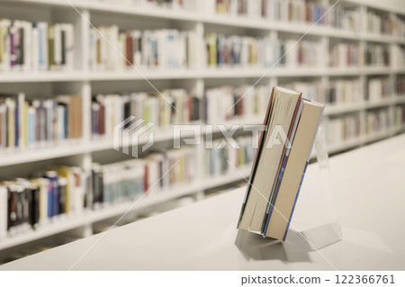 Open books rest on stand in bright library, background of blurred shelves filled with various books, reading atmosphere 122366761