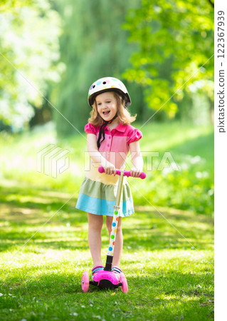 Little girl riding a colorful scooter Little girl riding a colorful scooter 122367939