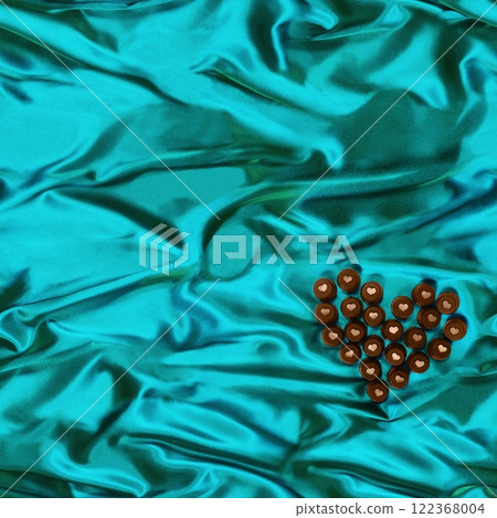 Seamless heart-shaped chocolate candy pattern on green-blue silk fabric background. 122368004