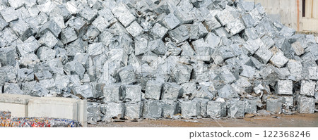 tacks of pressed aluminum cubes glisten in bright light, hinting at large-scale recycling operations. Reflective surfaces highlight an industrial push toward sustainability and efficient resource use 122368246