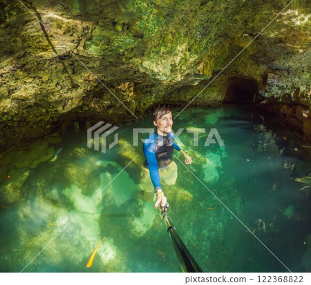 Man tourist in the water of a Mexican cenote surrounded by natural beauty. Adventure travel, eco-tourism, and exploration concept in a tropical paradise Man tourist in the water of a Mexican cenote surrounded by natural beauty. Adventure travel, eco-tourism, and exploration concept in a tropical paradise 122368822