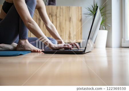 Low angle view of a woman sitting on a living room floor using and working on laptop computer 122369330