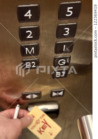 Person hand holding access key to move the elevator to a given floor making a gesture to the receiver. Floor numbers is displayed close-up 122369419