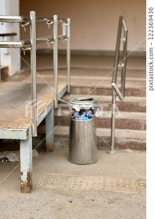 Overflowing trash can and scattered garbage on a sidewalk next to stairs next to supermarket 122369436
