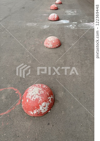 Red restrictive hemispheres on the asphalt road in the parking area of the car and the pedestrian area of walking people at the street. Area for foot people 122369448
