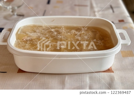 Aspic meat in the form of jelly is in a white container on the table during lunch in the home village. Close-up Aspic meat in the form of jelly is in a white container on the table during lunch in the home village. Close-up 122369487