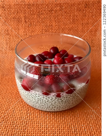 A lot of healthy Chia pudding with coconut milk in a glass containers can with fresh berries as cranberries, cranberry on light red background. Close-up A lot of healthy Chia pudding with coconut milk in a glass containers can with fresh berries as cranberries, cranberry on light red background. Close-up 122369490