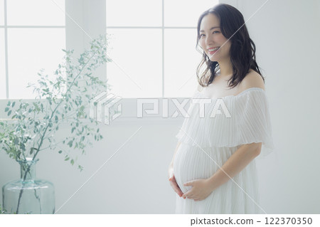 Pregnant woman standing by the window 122370350