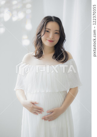 Pregnant woman standing by the window 122370355