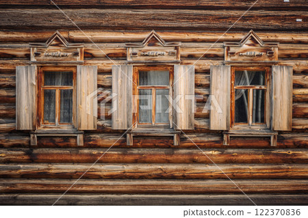 Close up of weathered wooden windows showcasing intricate carvings on a classic russian log house, capturing the essence of rural architecture Close up of weathered wooden windows showcasing intricate carvings on a classic russian log house, capturing the essence of rural architecture 122370836