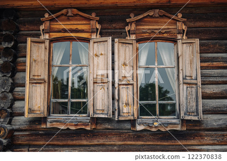 Open vintage wooden windows with carved architraves and slightly open shutters on a traditional russian log cabin 122370838