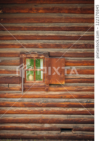 Traditional russian log cabin showcasing weathered wooden wall with a small, partially opened window revealing a vase of flowers inside Traditional russian log cabin showcasing weathered wooden wall with a small, partially opened window revealing a vase of flowers inside 122370845