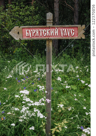 Weathered wooden signpost marking buryat village direction, nestled amid wildflowers in lush siberian woodland landscape 122370856