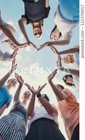 School friends joining hands to form heart shape against cloudy sky, representing unity, friendship, and teamwork 122370917