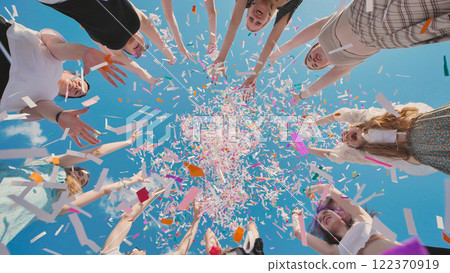 Group of high school students throwing colorful confetti in the air celebrating graduation under a blue sky 122370919