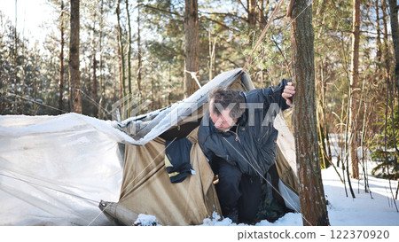 Homeless alcohol addicted man leaving his makeshift tent in a snowy forest, struggling with addiction and poverty 122370920