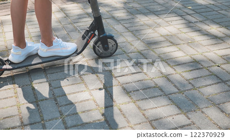 Teenage girl riding electric scooter along sunny park pathway, wearing casual summer outfit Teenage girl riding electric scooter along sunny park pathway, wearing casual summer outfit 122370929