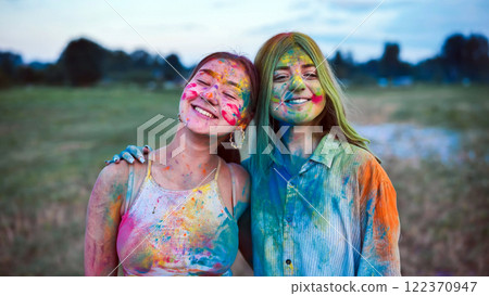 Two happy young women embrace, covered in vibrant holi colors, celebrating friendship and the joy of the festival 122370947