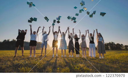 Group of cheerful high school students throwing books in the air celebrating summer vacation in a field at sunset 122370970