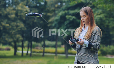 Businesswoman piloting a drone in a park, holding a remote control and navigating the aircraft through the air 122371021