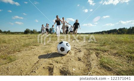 Adolescents happily playing on a lush green meadow, pursuing a soccer ball in the sunshine on a bustling summer day 122371041