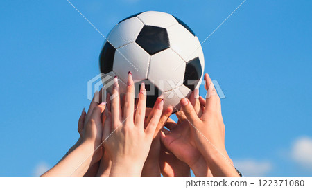 Many hands holding a soccer ball against a blue sky, symbolizing teamwork, friendship, and sportsmanship in school 122371080