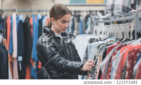 Shopper browsing trendy clothing, carefully examining garments on racks and weighing fashion choices in stylish retail environment 122371091