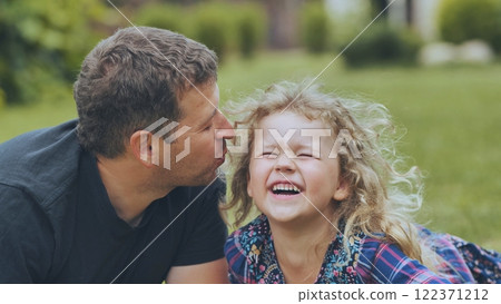 Loving dad tenderly kissing giggling daughter's cheek, sharing warm moment during outdoor family gathering 122371212