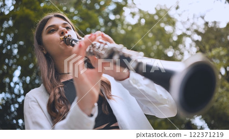 Young musician performing clarinet amid lush green park, expressing melodic passion surrounded by tranquil natural landscape 122371219