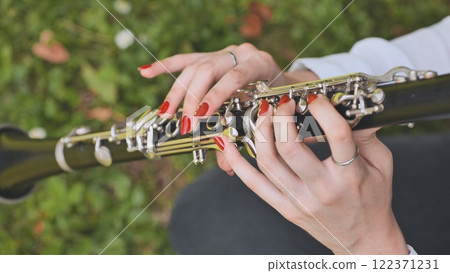 Female clarinetist performing with vibrant red nails, surrounded by verdant foliage, expressing musical artistry in tranquil garden landscape 122371231