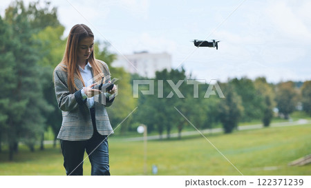 Professional woman flying drone with remote control in park, demonstrating technological innovation among green landscape 122371239