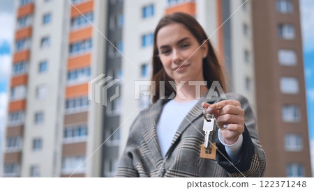 Realtor handing over apartment keys to smiling client, symbolizing successful property transaction near contemporary residential structure 122371248
