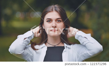 Beautiful georgian woman holding flowing hair, standing gracefully amid lush greenery, embodying natural elegance and feminine charm 122371296