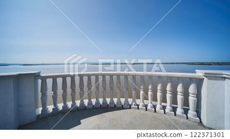 Marble terrace with ornate balusters framing serene lake waters, reflecting cloudless sky and radiating tranquil landscape atmosphere in Khabarovsk. 122371301