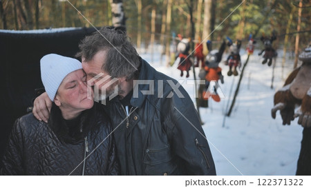 Alcohol addicted homeless couple embracing in snowy woods with hanging mickey mouse and other plush toys in the background Alcohol addicted homeless couple embracing in snowy woods with hanging mickey mouse and other plush toys in the background 122371322