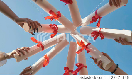 Students are celebrating their graduation by holding their diplomas up in the air forming a circle. Students are celebrating their graduation by holding their diplomas up in the air forming a circle. 122371356