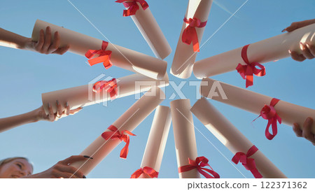Students are celebrating their graduation by holding their diplomas up in the air forming a circle. Students are celebrating their graduation by holding their diplomas up in the air forming a circle. 122371362