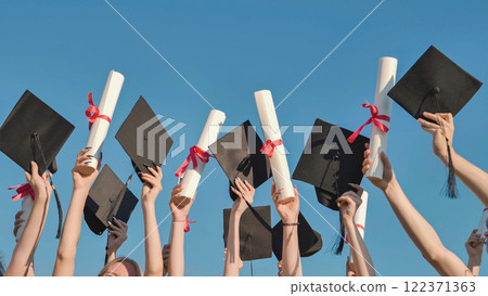 Group of students celebrating graduation by raising their diplomas and mortarboards to the sky 122371363