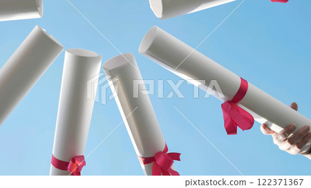 Group of graduates joyfully tossing their diplomas in the air under a clear blue sky Group of graduates joyfully tossing their diplomas in the air under a clear blue sky 122371367