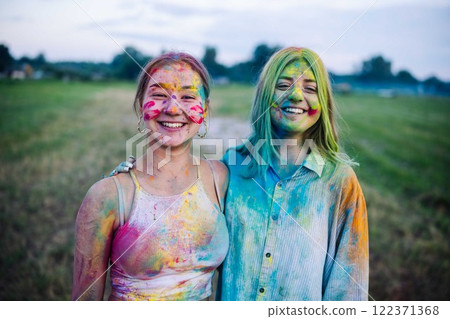 Two young women, covered in colorful powder, embrace and smile during the holi festival celebration Two young women, covered in colorful powder, embrace and smile during the holi festival celebration 122371368
