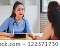 Female nurse jotting down health information during a consultation with a patient, dedicated medical care. 122371730