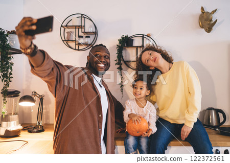 Stylish happy diverse couple with little daughter taking selfie while in kitchen 122372561